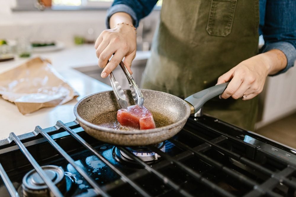 A cook searing food in a pan on the stove